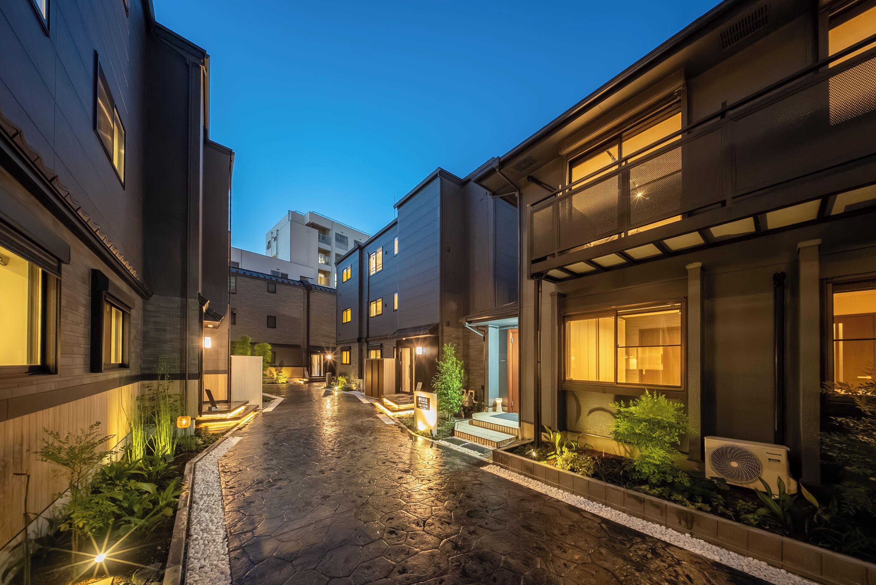 A modern building with a paved courtyard, outdoor lighting, and a visible air conditioning unit.