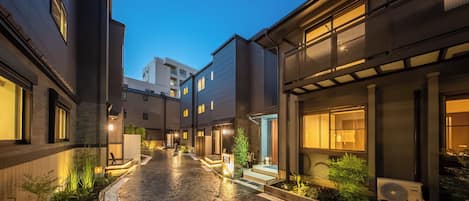 A modern building with a paved courtyard, outdoor lighting, and a visible air conditioning unit.