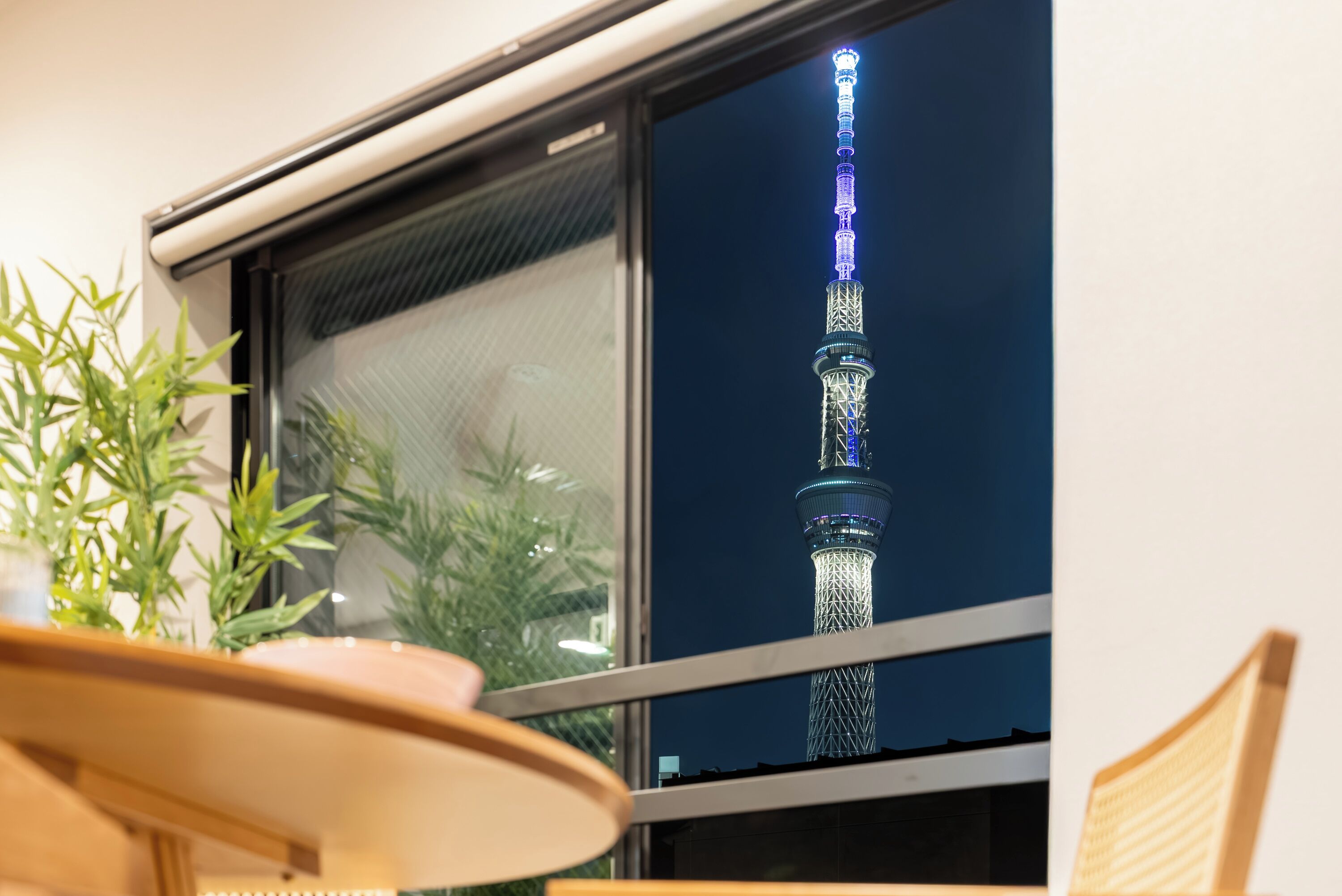 Vista de la Torre de Tokio a través de una ventana, con una planta en maceta sobre una mesa en primer plano.