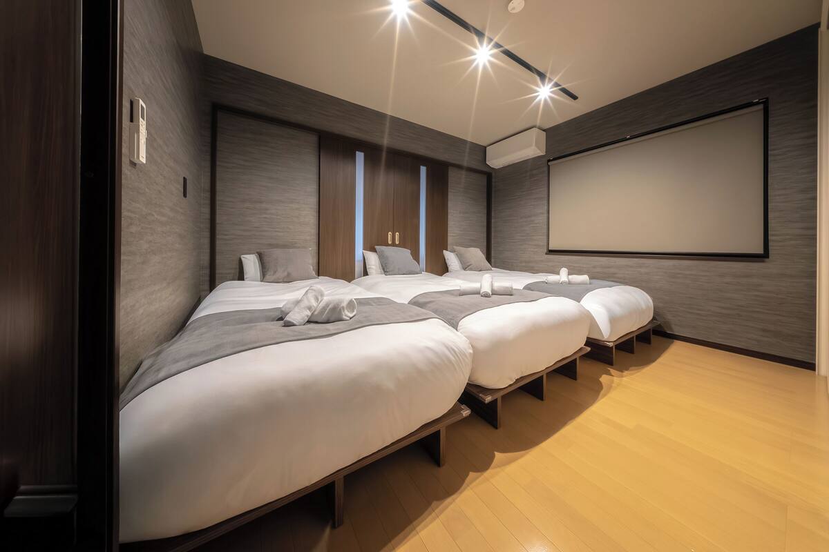 Habitación de hotel con tres camas, una pantalla grande y suelo de madera.