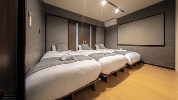 A hotel room with three beds, a large screen, and a wooden floor.