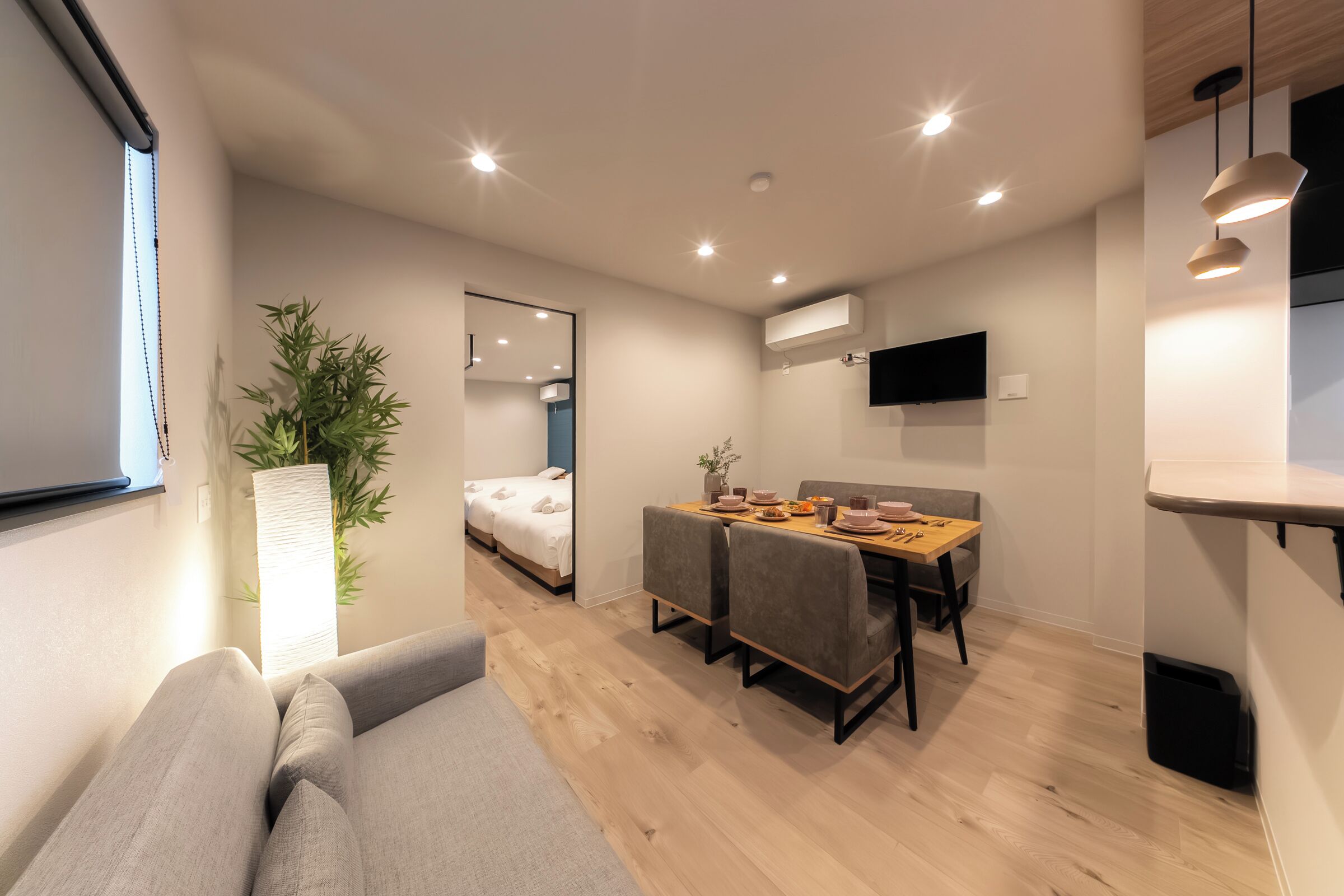 A modern room with a sofa, a dining table with chairs, a mirror, a TV, and a potted plant.