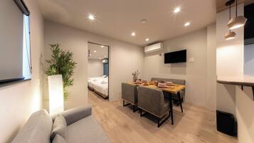 A modern room with a sofa, a dining table with chairs, a mirror, a TV, and a potted plant.