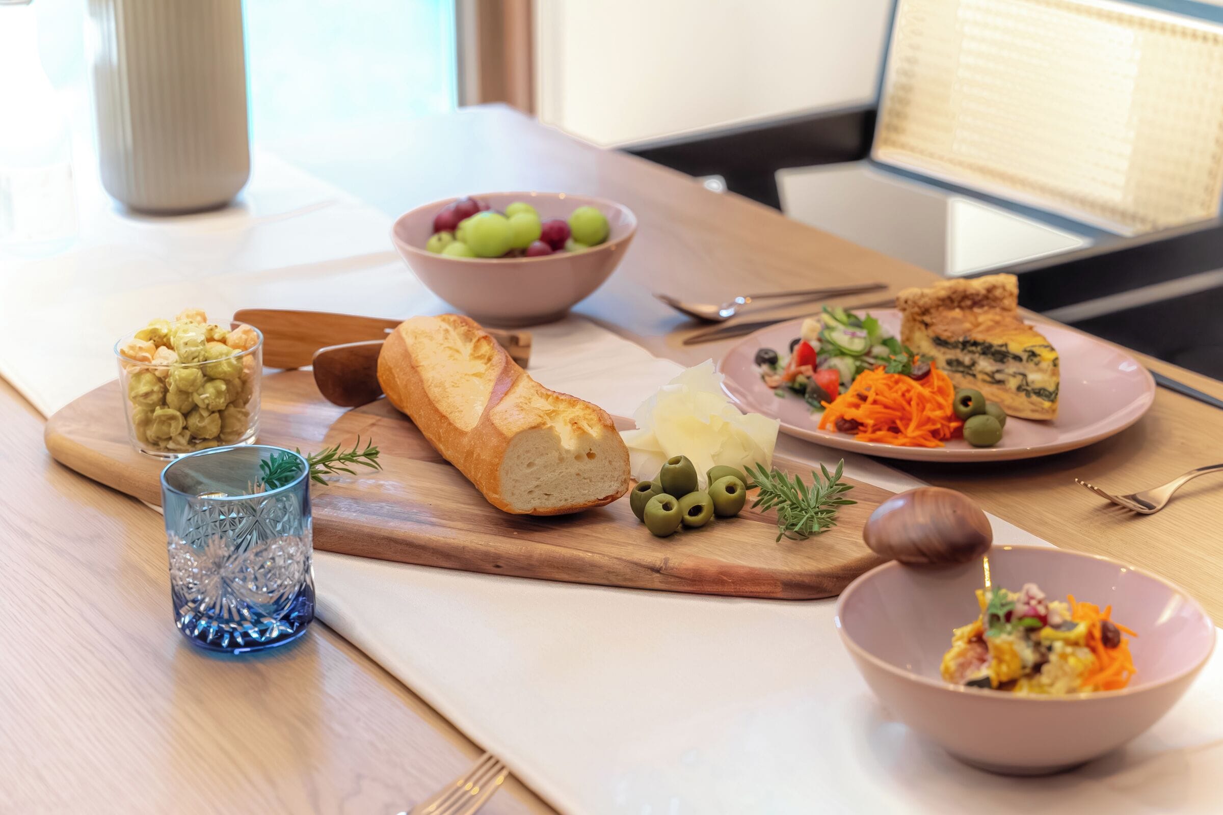 Una mesa con comida, un bol de uvas, un vaso de bebida y una tabla de madera.
