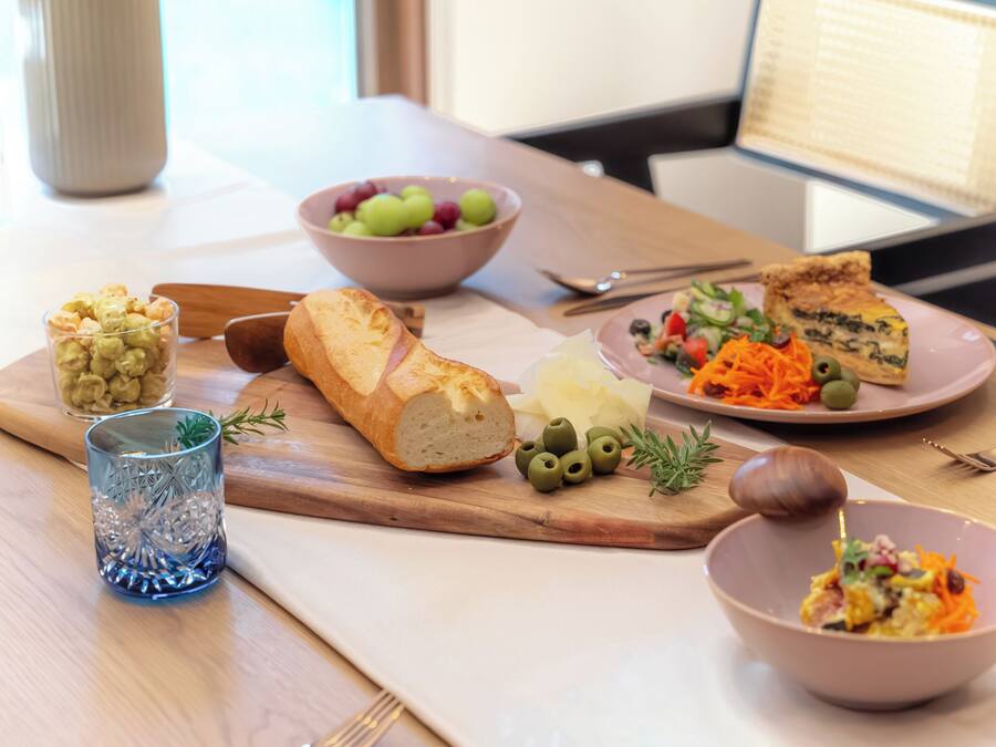 A table with food items, a bowl of grapes, a glass of a beverage, and a wooden cutting board.
