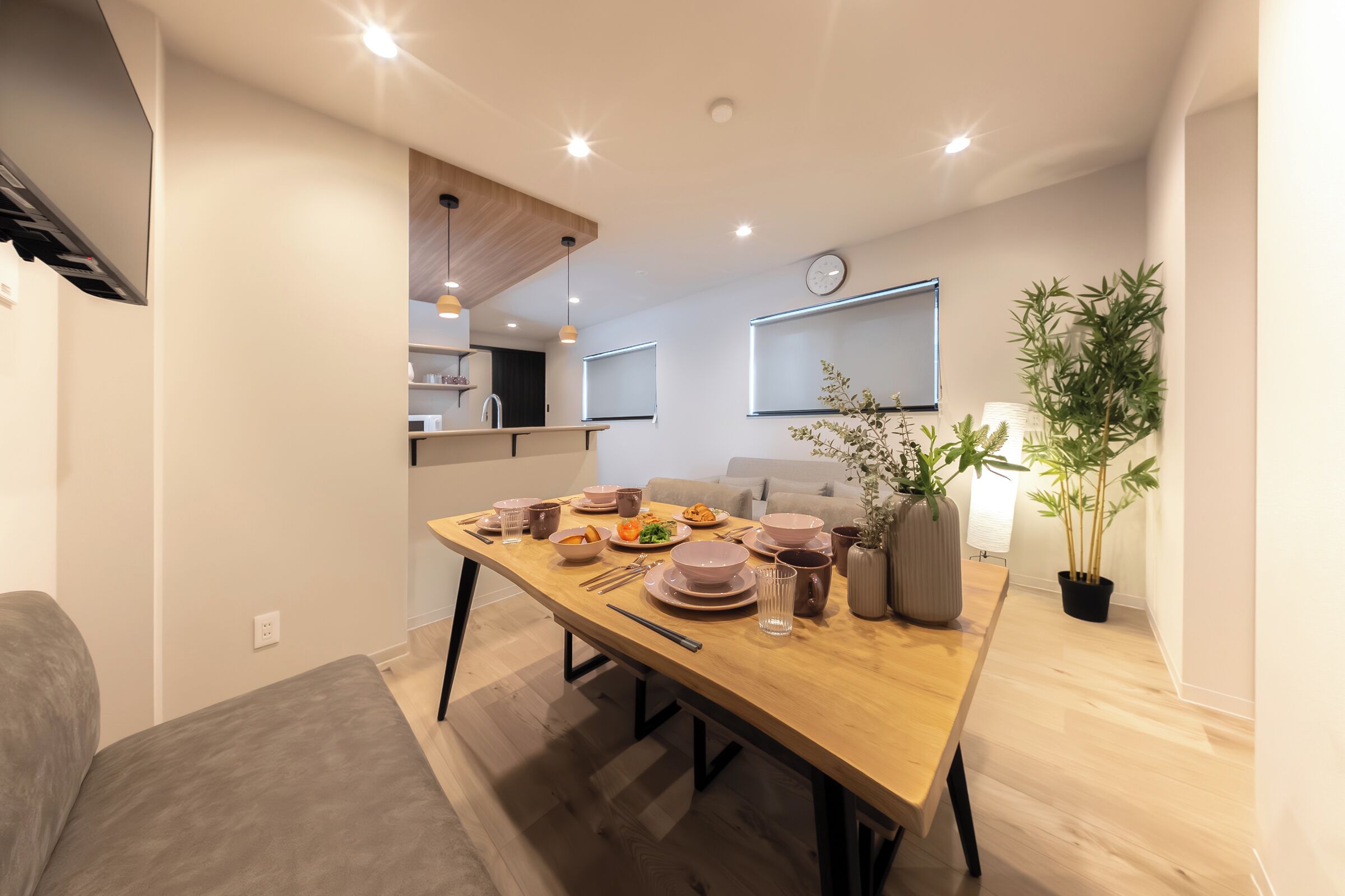 Un comedor moderno con una mesa de madera dispuesta para una comida, un sofá y una planta en maceta.