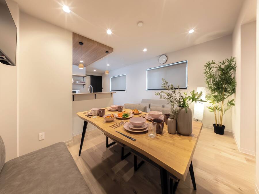 Un comedor moderno con una mesa de madera dispuesta para una comida, un sofá y una planta en maceta.