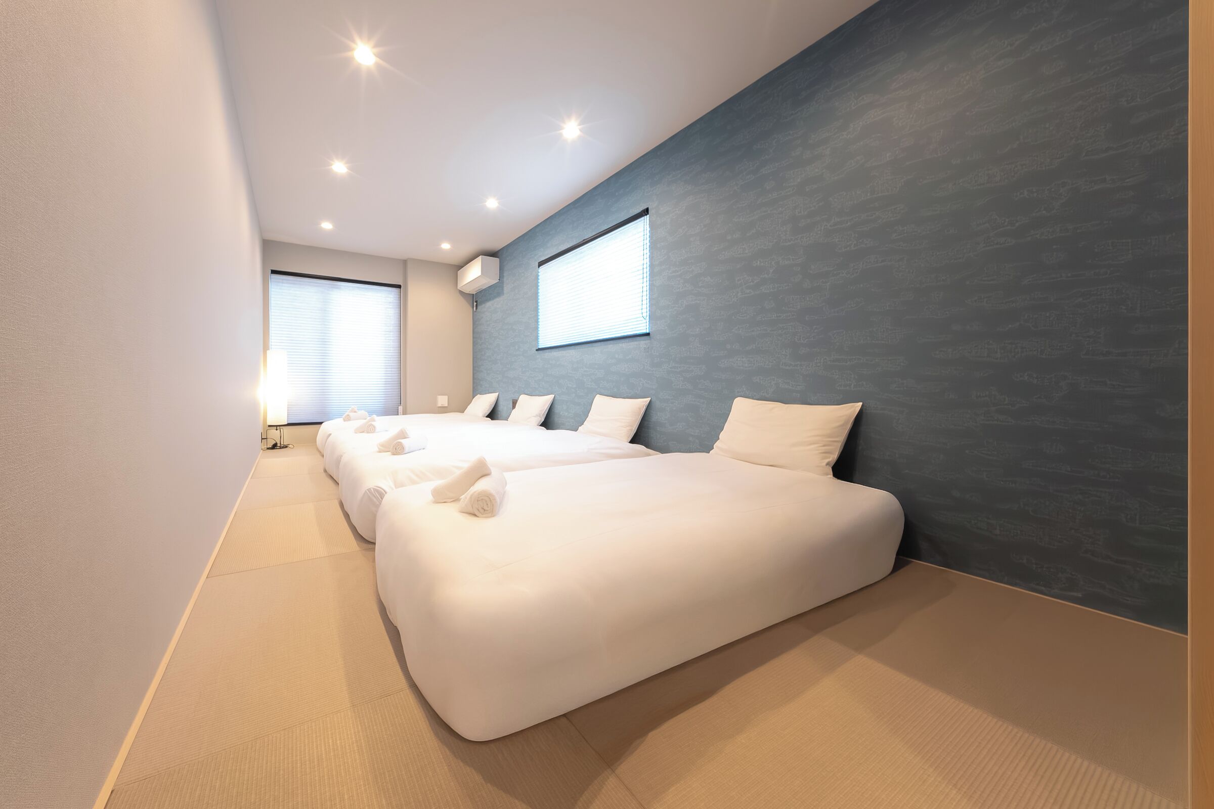 Ein modernes Hotelzimmer mit drei Betten, einem großen Fenster und einer Wand mit dunkler Struktur.