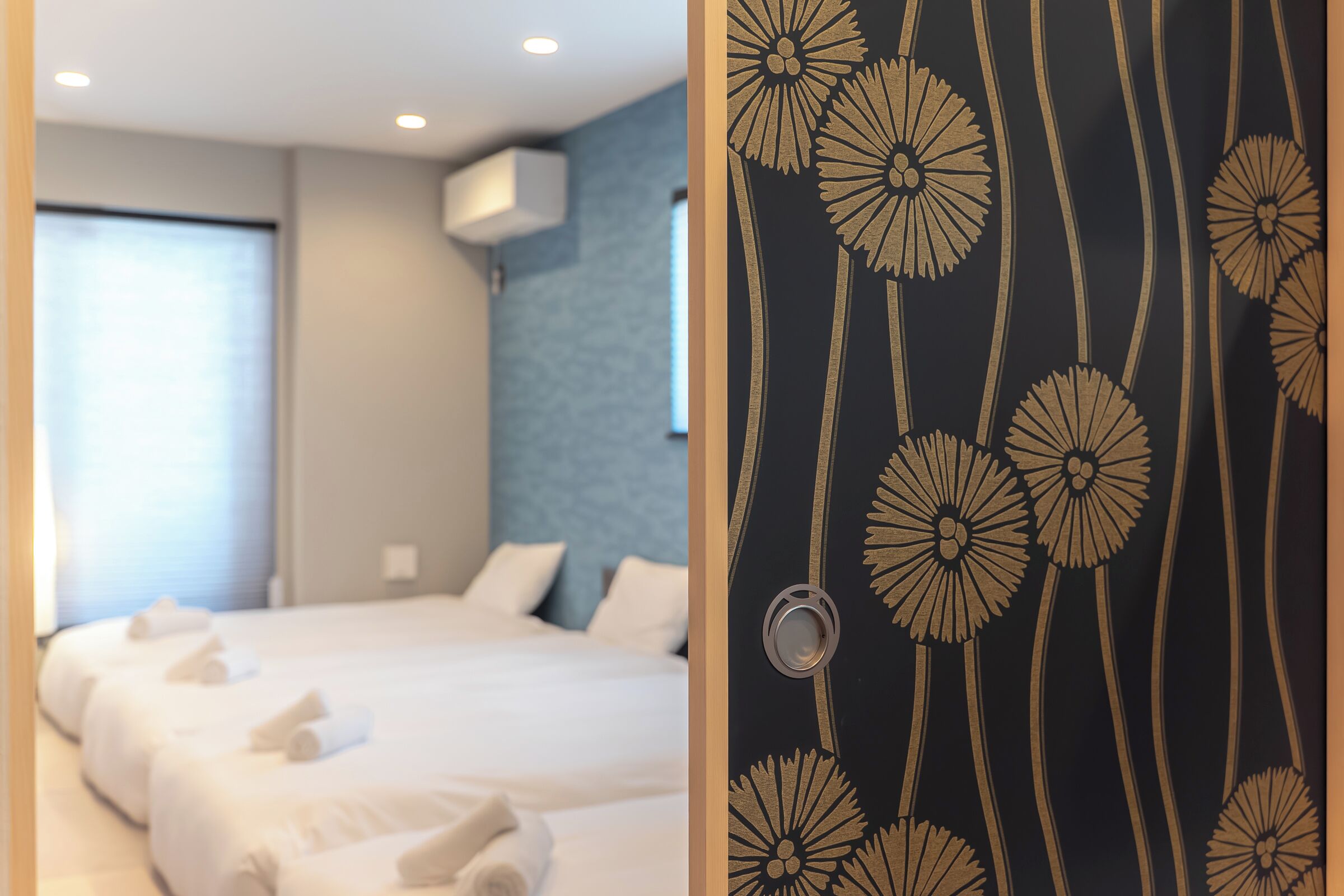 A hotel room with a bed, a window, and a wall with a floral pattern.