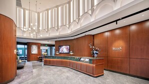 Ein Hotel-Empfangsbereich mit einer gebogenen Rezeption, Holzvertäfelung, einem Flachbildfernseher und einem großen Fenster.