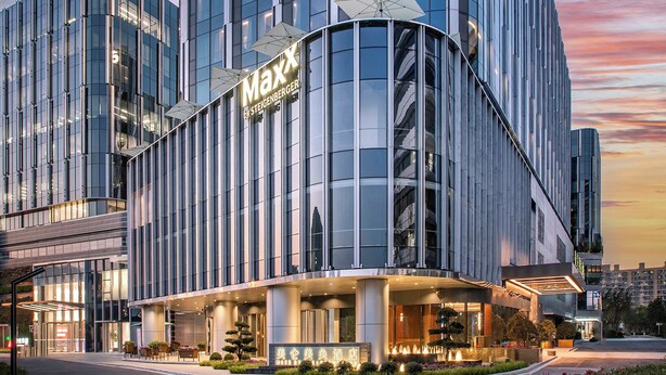 Ein modernes Hotel mit einer geschwungenen Fassade, großen Fenstern und einem auffälligen 'Maxx'-Schild.