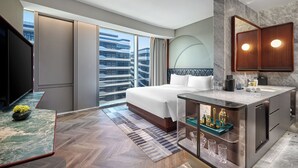 Ein modernes Hotelzimmer mit einem großen Bett, einem Schminktisch mit Spiegel, einem Fernseher und Blick auf die Stadt.