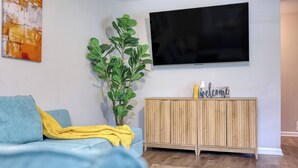 Ein Wohnzimmer mit einer Couch, einem Fernseher, einem Holzschrank und einer Pflanze.