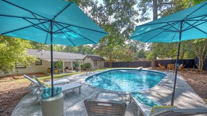 Ein Garten mit Schwimmbad, Liegestühlen und Sonnenschirmen.