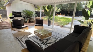 Eine Terrasse im Freien mit einer Rattan-Couch, einem Glastisch und einem Grill.