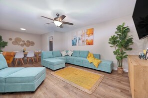 A living room with a sectional sofa, a coffee table, a dining table with chairs, a ceiling fan, and wall art. - Kings w/Pool & Grill, 15 mins to Fort Benning (Columbus)