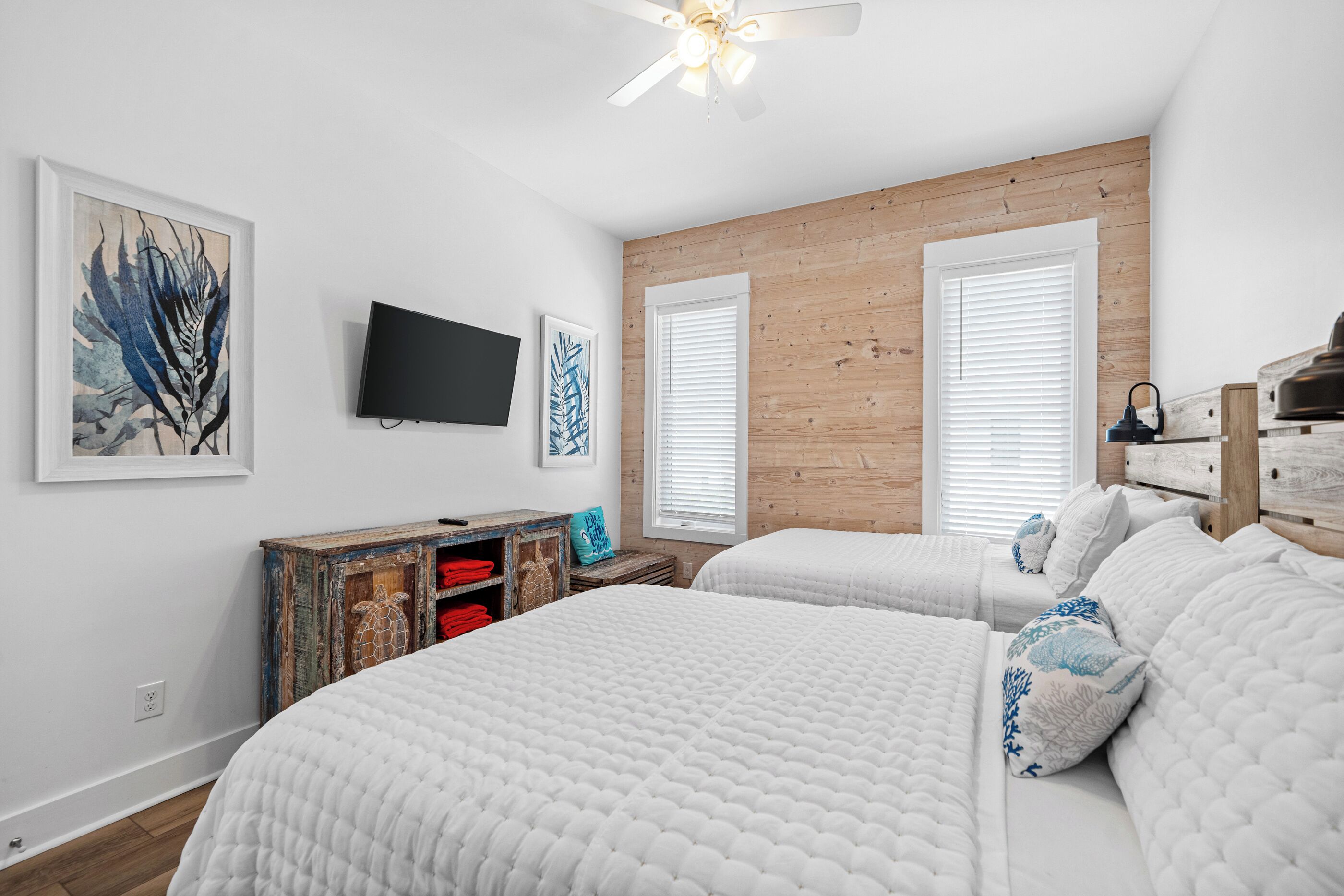 Ein Schlafzimmer mit zwei Betten, einem Fernseher, Holzwänden und Bildern an der Wand.