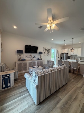 A modern living room with a striped sofa, a television, and a ceiling fan. - August Dates Available-Key Lime Cottage-Pet Friendly-Snowbird Wanted!! (Orange Beach)