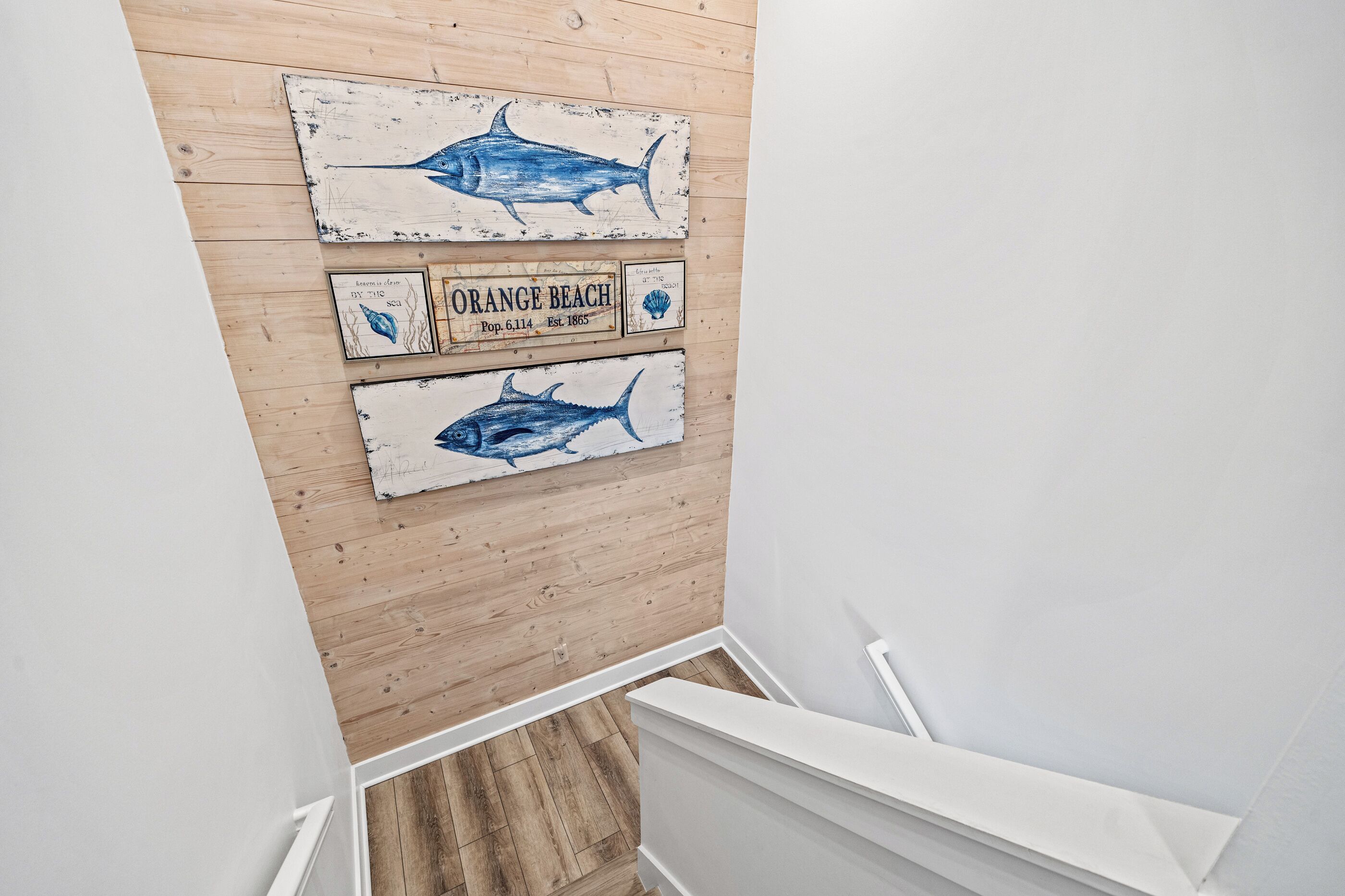 A wooden wall with three nautical-themed signs, a white staircase, and a wooden floor.