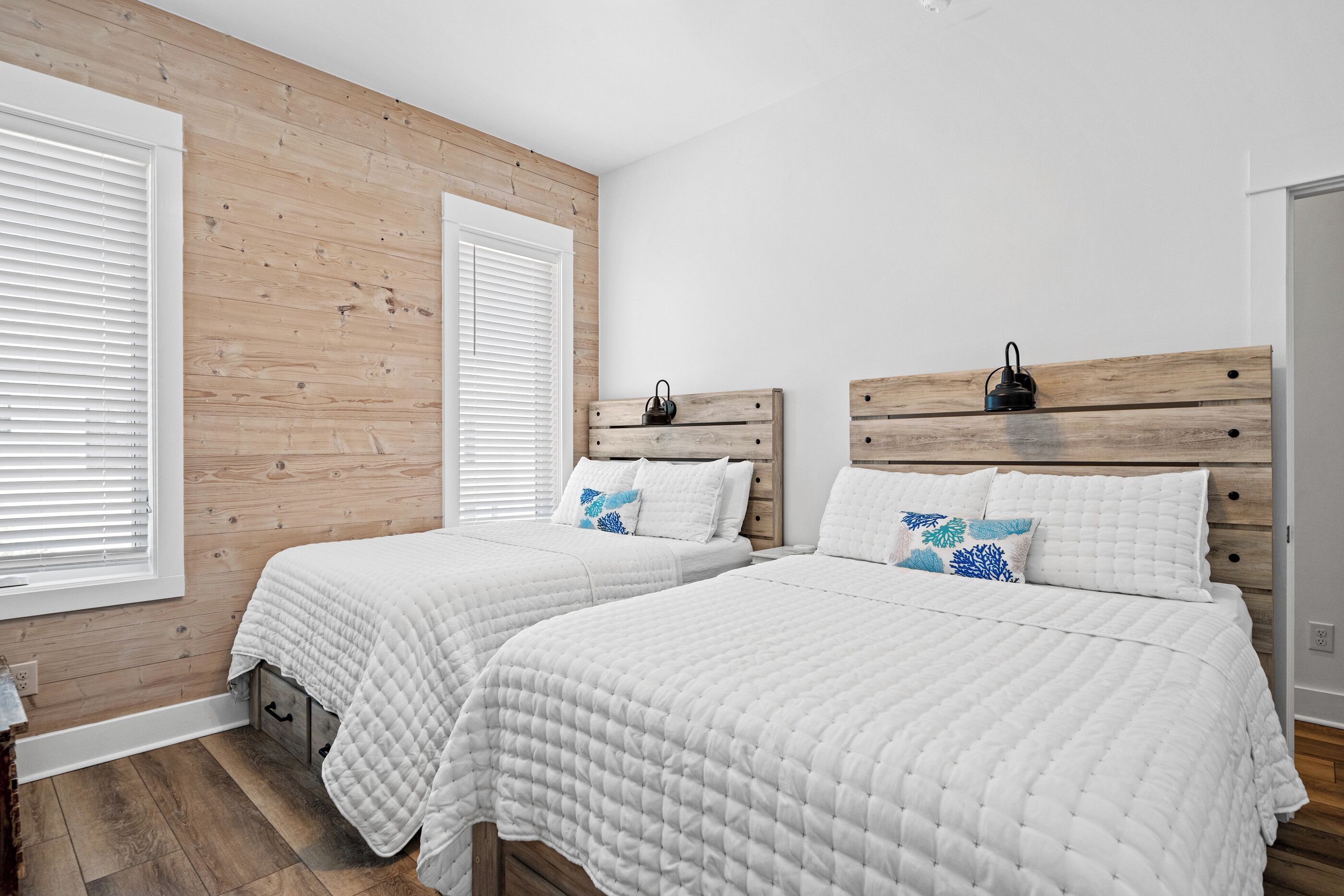 A bedroom with two beds, wooden headboards, white bedding, and a wooden wall.
