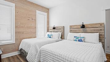 Une chambre avec deux lits, des têtes de lit en bois, du linge de lit blanc et un mur en bois.
