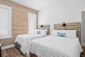 A bedroom with two beds, wooden headboards, white bedding, and a wooden wall.