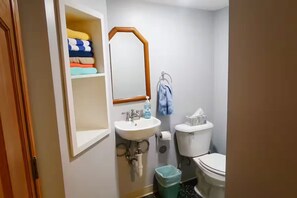 Un baño con lavamanos blanco, espejo, inodoro y un cubo de basura.