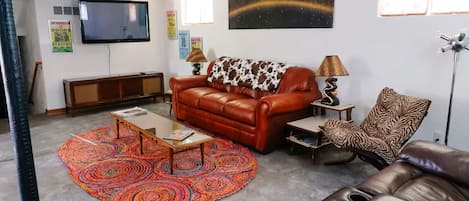 Una sala de estar con un sofá de cuero marrón, un tapete estampado, un televisor montado en la pared y una silla con estampado de cebra.