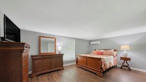 A bedroom with a wooden dresser, a bed with floral bedding, a nightstand with a lamp, and a large mirror.
