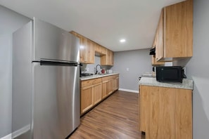 Una cocina con armarios de madera, un refrigerador de acero inoxidable, un microondas y un lavamanos.