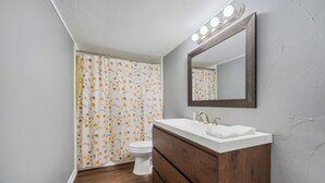 Une salle de bain avec un meuble-lavabo en bois, un lavabo blanc, un miroir avec éclairage intégré et des toilettes.