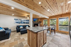 A spacious living area with a fireplace, a stone-tiled floor, and a large wooden ceiling.