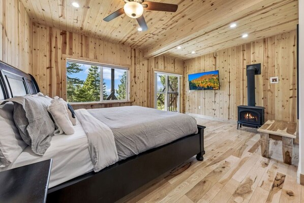 A wooden cabin bedroom with a bed, a fireplace, and a large window.