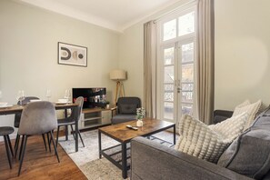 A living room with a sofa, a coffee table, a TV, and a dining area with chairs and a table. - Chelsea 2BR Flat with Balcony • Fulham Broadway 7min (Greater London)