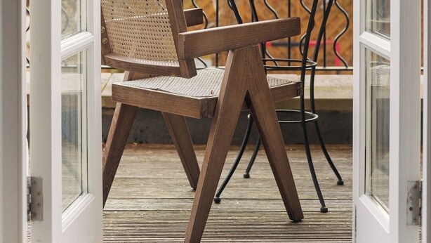Une porte ouverte donnant sur un balcon où se trouvent une chaise en bois et une petite table.