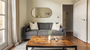 Un salon avec un canapé gris, une table basse en bois, un miroir et une porte donnant sur une autre pièce.