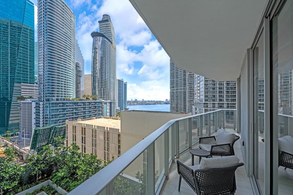 A balcony with outdoor furniture, a view of high-rise buildings, and a body of water in the distance. - Exclusive 2BR in Brickell-Views & Top Amenities-Monthly Stay (Miami)