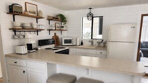 A kitchen with white cabinetry, a central island with stools, a microwave, a stove, and a refrigerator. - Spacious cozy, comfy home in The Poconos, private community of The Hideout (Hamlin)