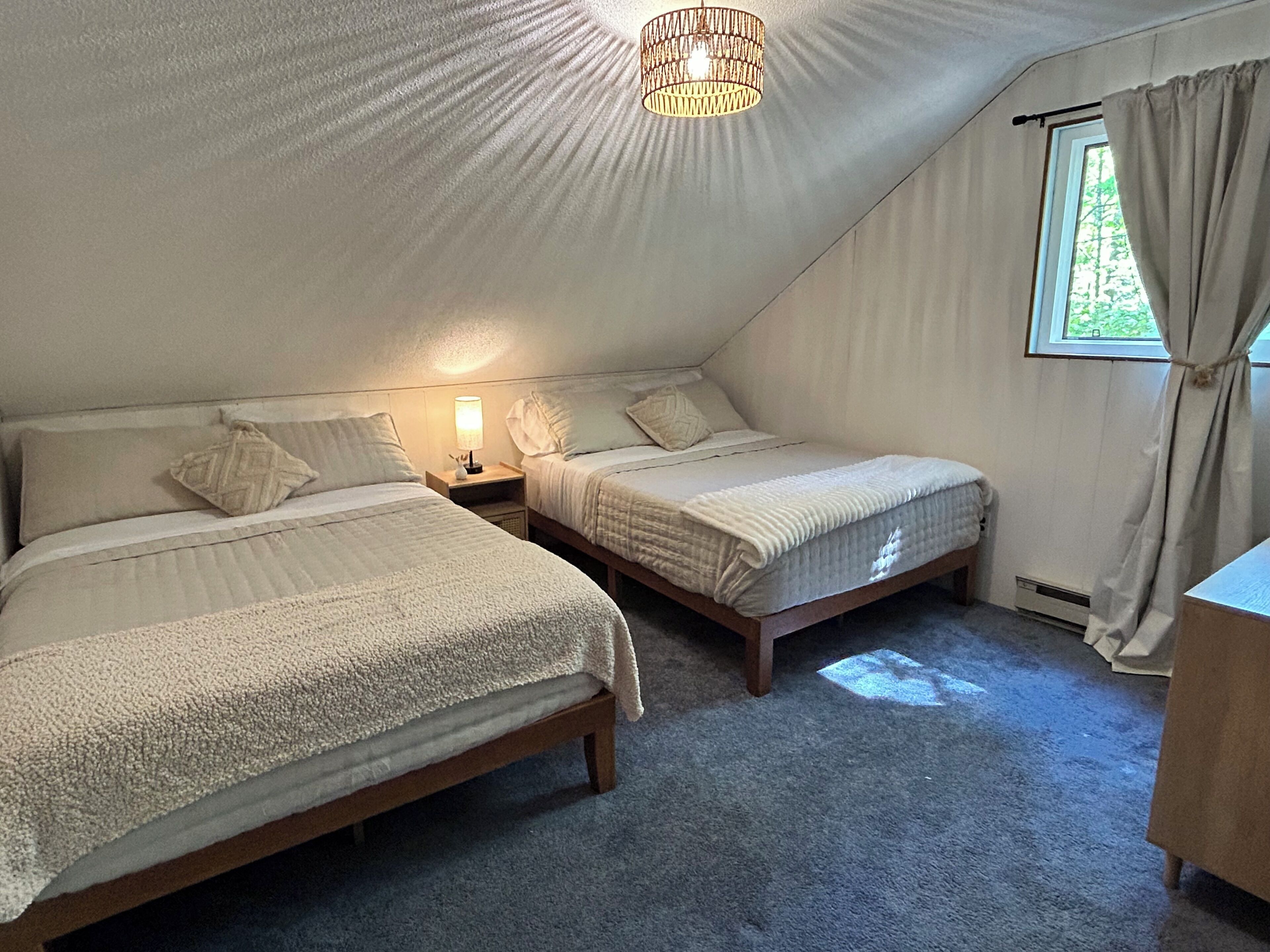 Une chambre avec deux lits, une table de chevet avec une lampe, une fenêtre avec des rideaux et un luminaire au plafond.