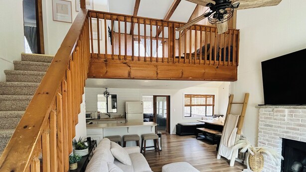 A loft-style living area with a wooden staircase, a sofa, a fireplace, and a kitchen in the background. - Spacious cozy, comfy home in The Poconos, private community of The Hideout (Hamlin)