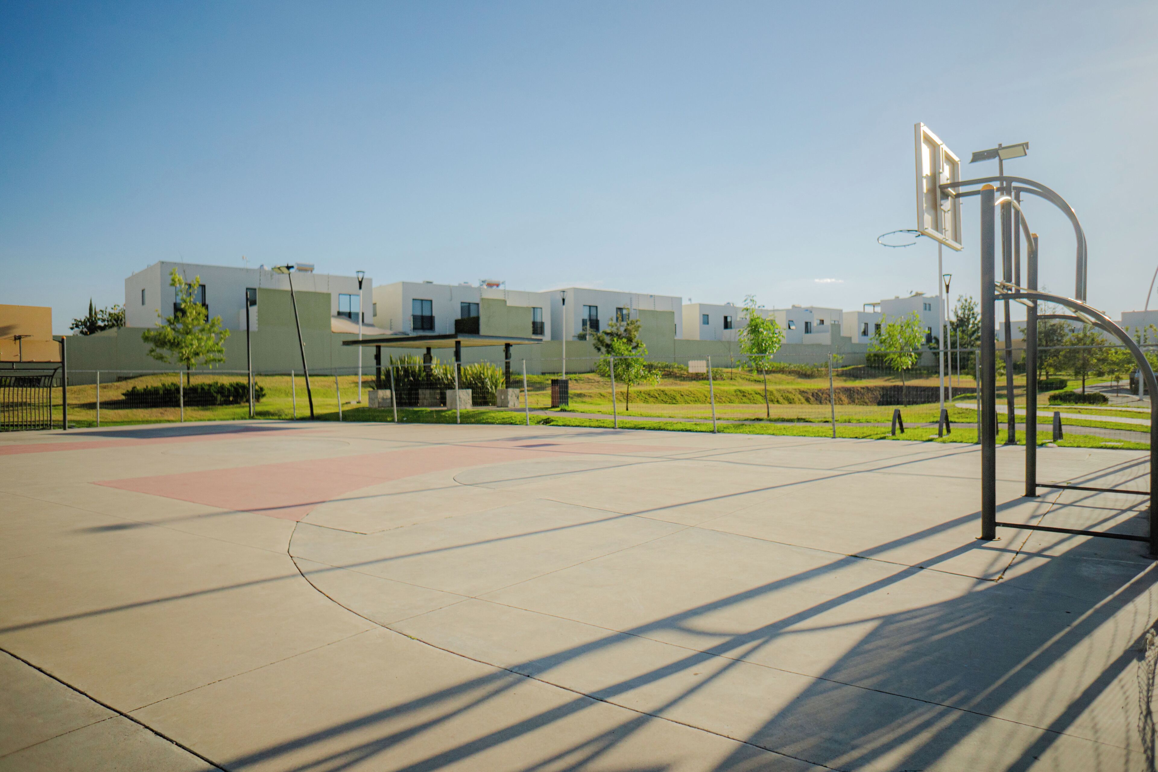 Een basketbalveld met een basket, een hek en moderne gebouwen op de achtergrond.