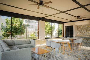 Une pièce moderne comprenant un canapé, une table, des chaises, un ventilateur de plafond, de grandes fenêtres et un mur recouvert de carreaux.