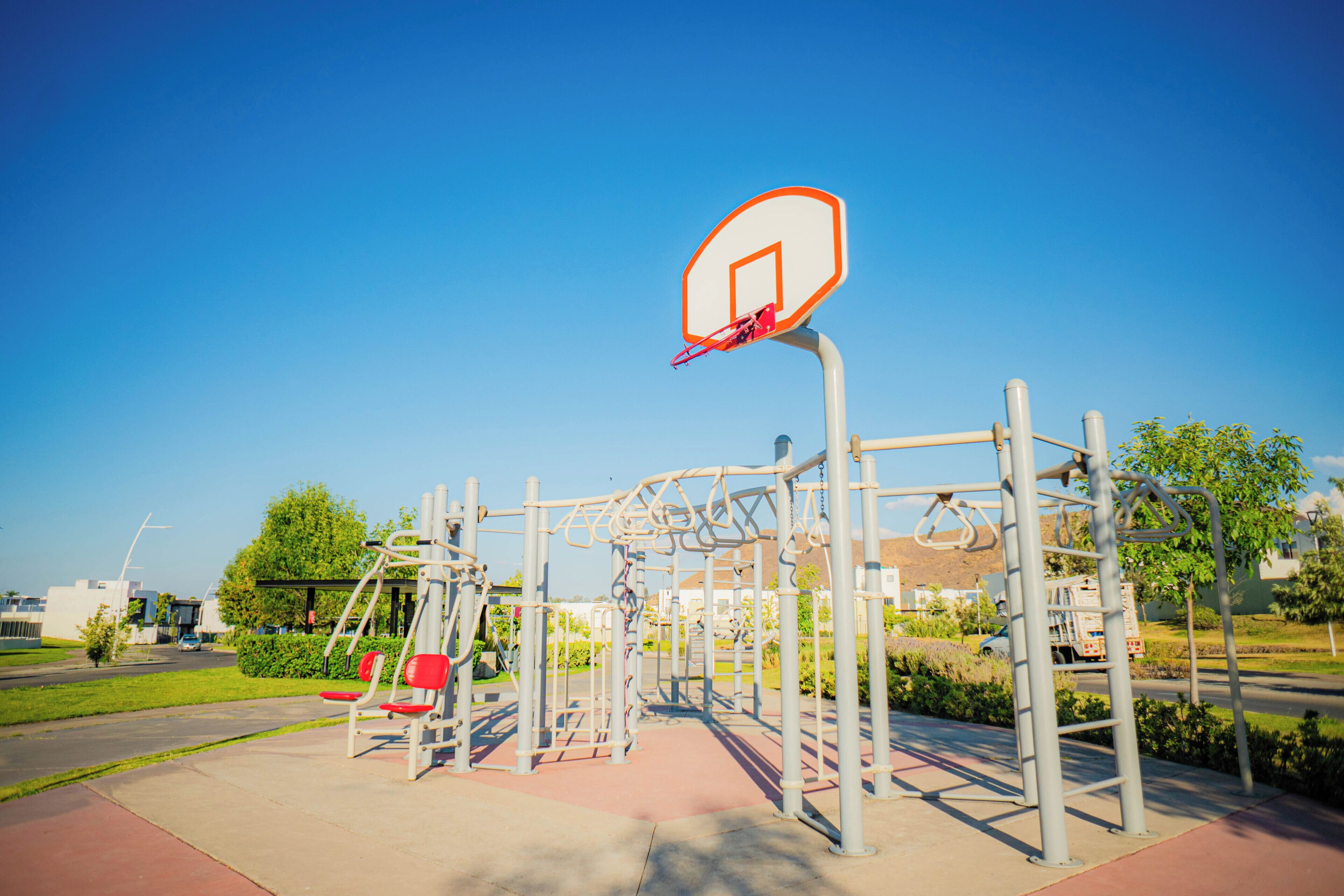 Une aire de jeux avec un panier de basket, des structures d’escalade et un banc rouge.