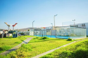 Un bâtiment moderne doté d’une façade en verre, une aire de jeux avec des toboggans et un ciel dégagé.