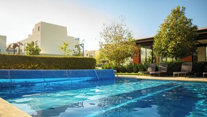 Ein Schwimmbecken mit klarem Wasser, umgeben von einer Hecke, und ein Gebäude mit moderner Architektur im Hintergrund.