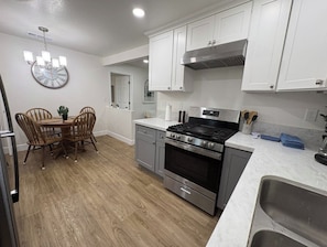 Una cocina moderna con armarios blancos, una estufa de acero inoxidable y un comedor con sillas de madera.