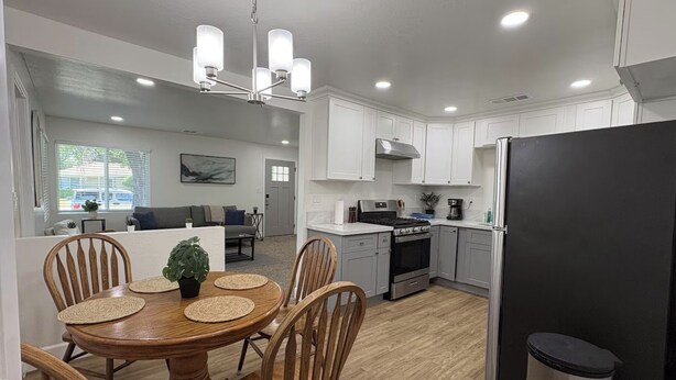 Una cocina moderna con armarios blancos, un refrigerador negro y un comedor con sillas de madera y una mesa redonda.