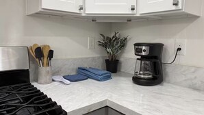 Una cocina con armarios blancos, estufa, cafetera y planta en maceta.