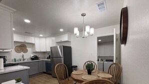 Una cocina moderna con armarios blancos, un refrigerador de acero inoxidable, una mesa de comedor con cuatro sillas y una lámpara colgante.
