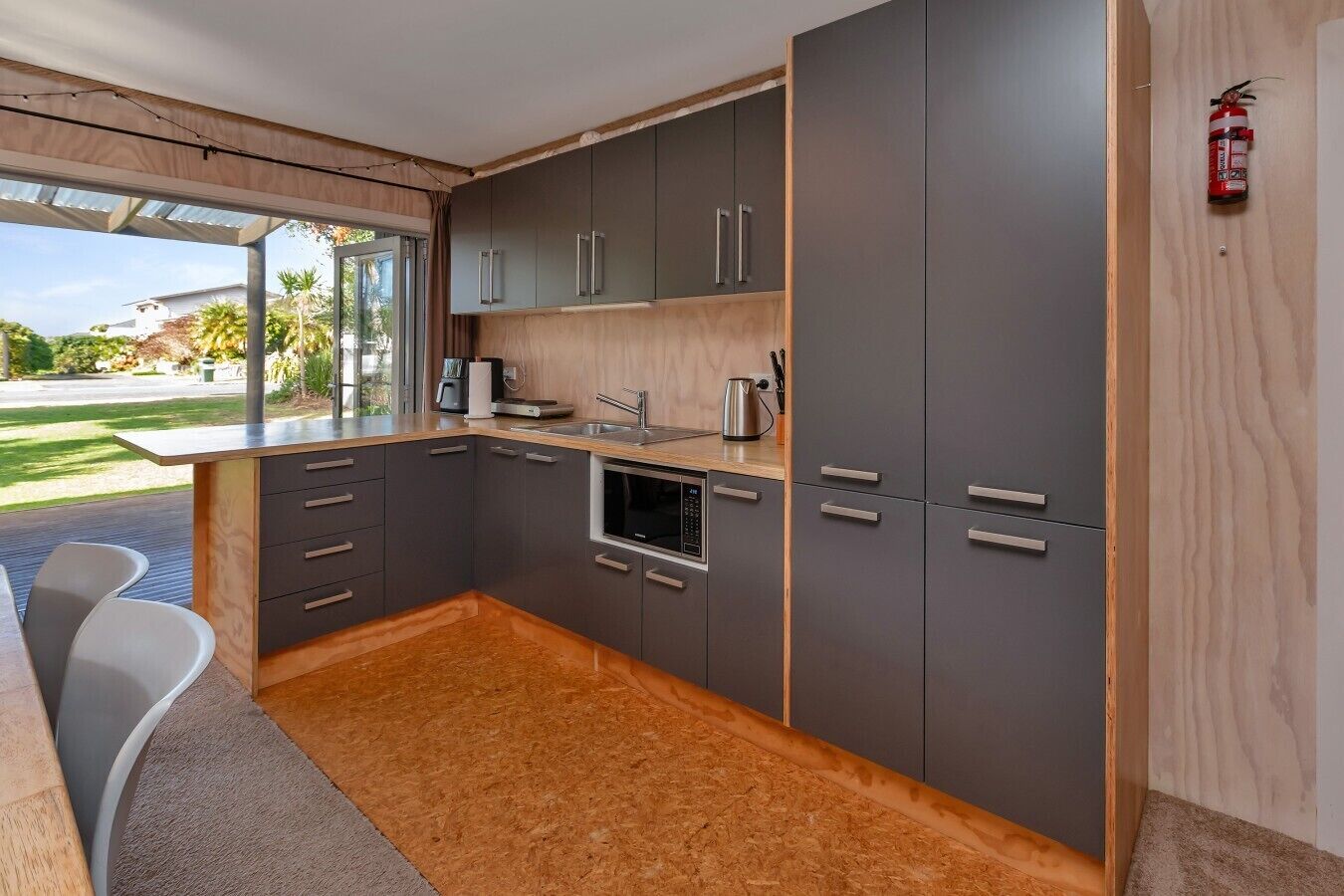 A modern kitchen with grey cabinets, a built-in oven, and a coffee maker.